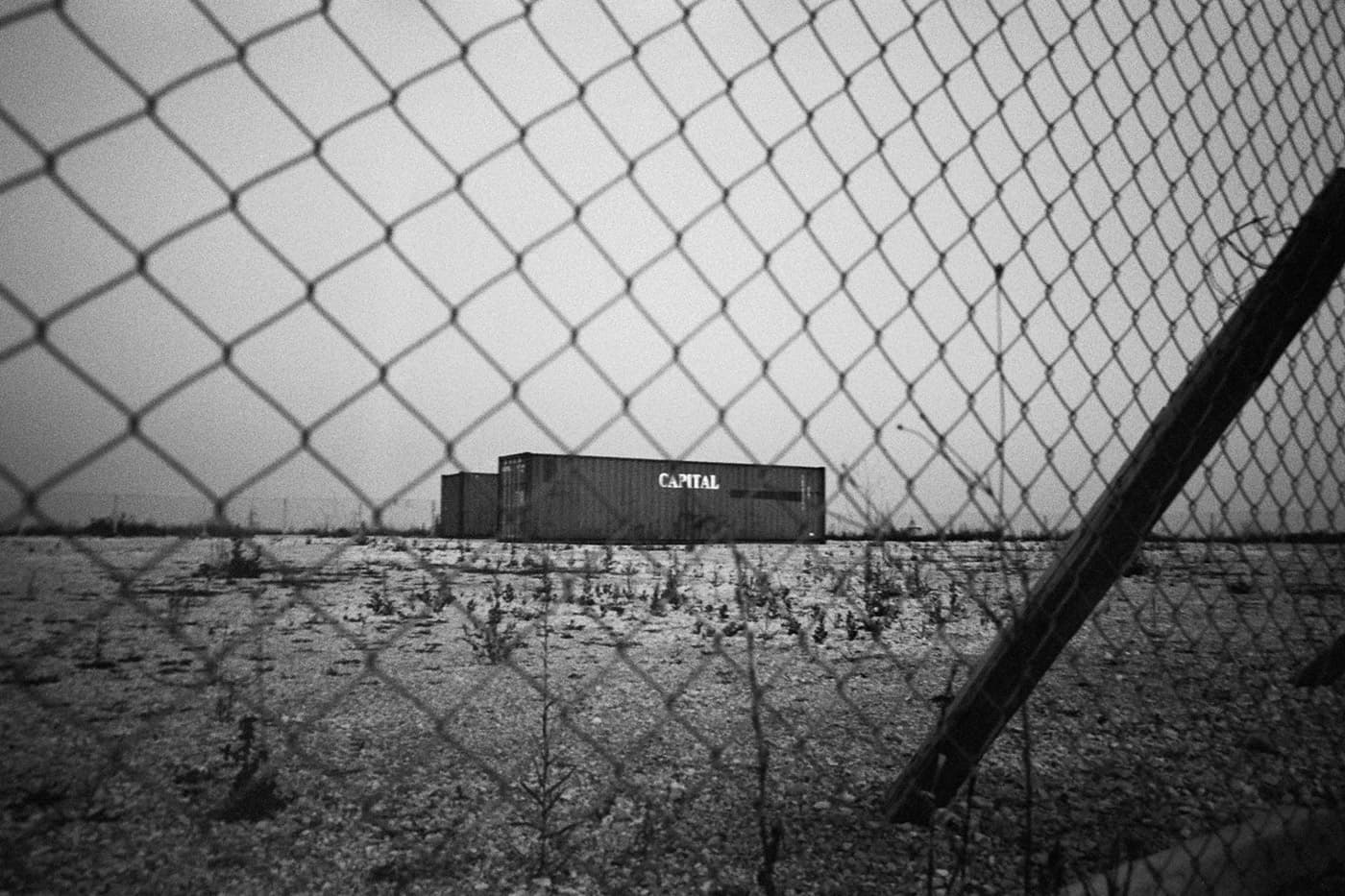 A fenced large area with metal shipping containers in the middle, one with a sign reading “capital”.