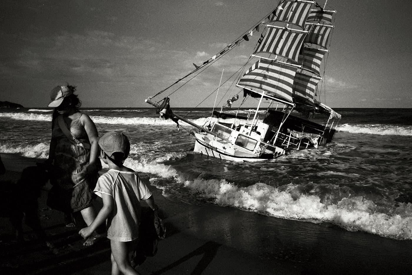 Black and white photograph of a sinking ship near the coast with people on the shore