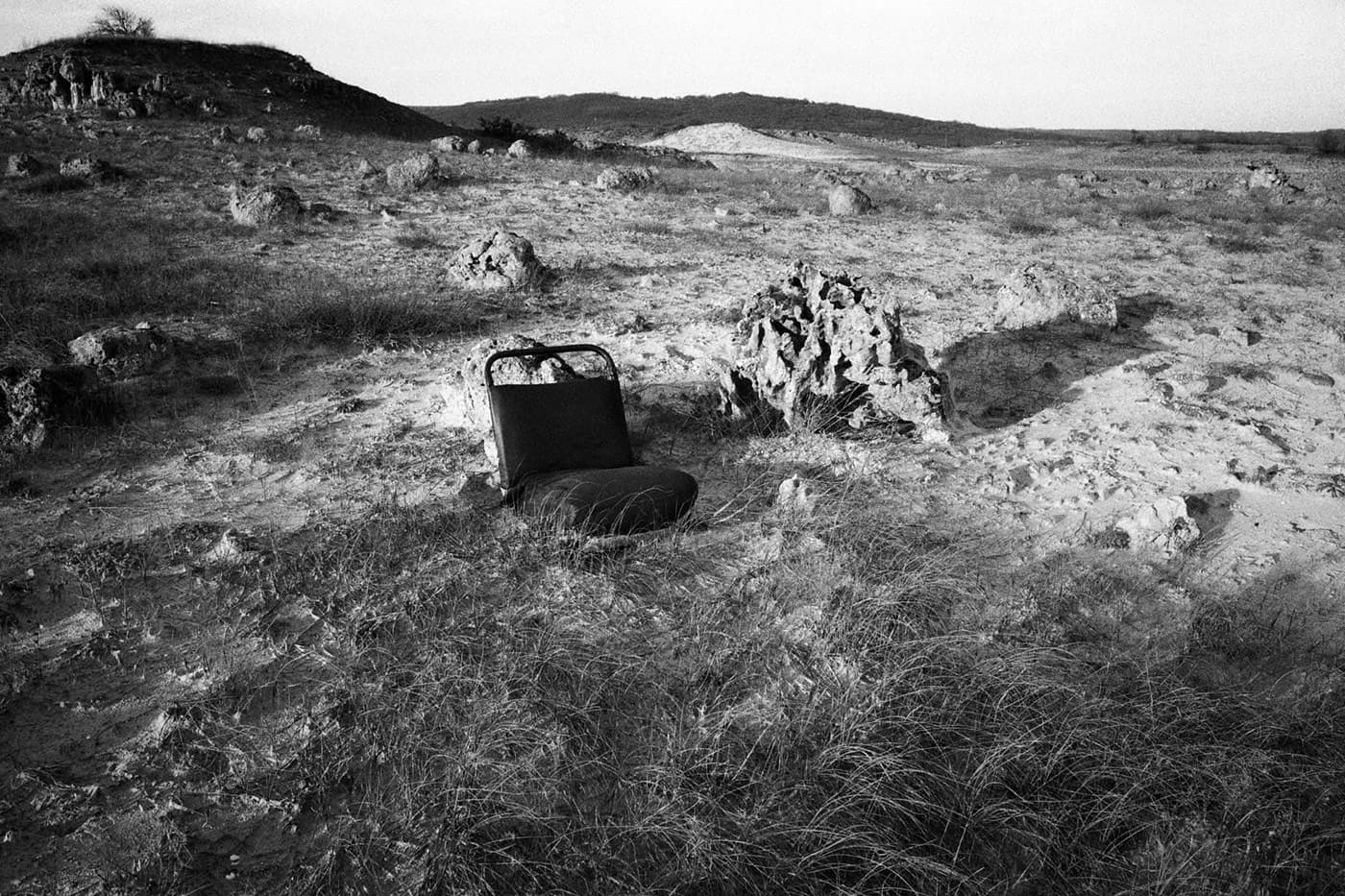 An old, abandoned bus or car seat sitting alone in a rocky, deserted field.
