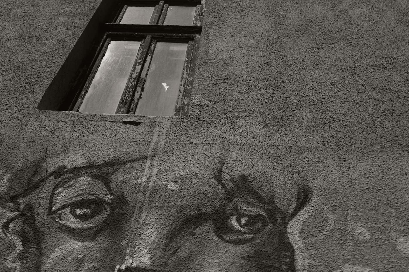Building facade with a window above a street stencil of a human face and eyes