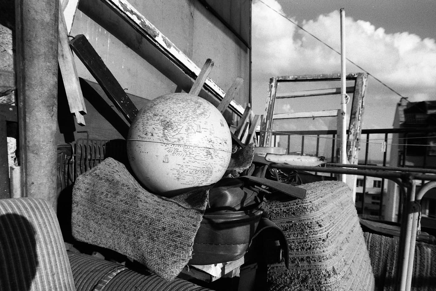 A city terrace with scattered objects and old items, with a plastic globe of the Earth placed on top.