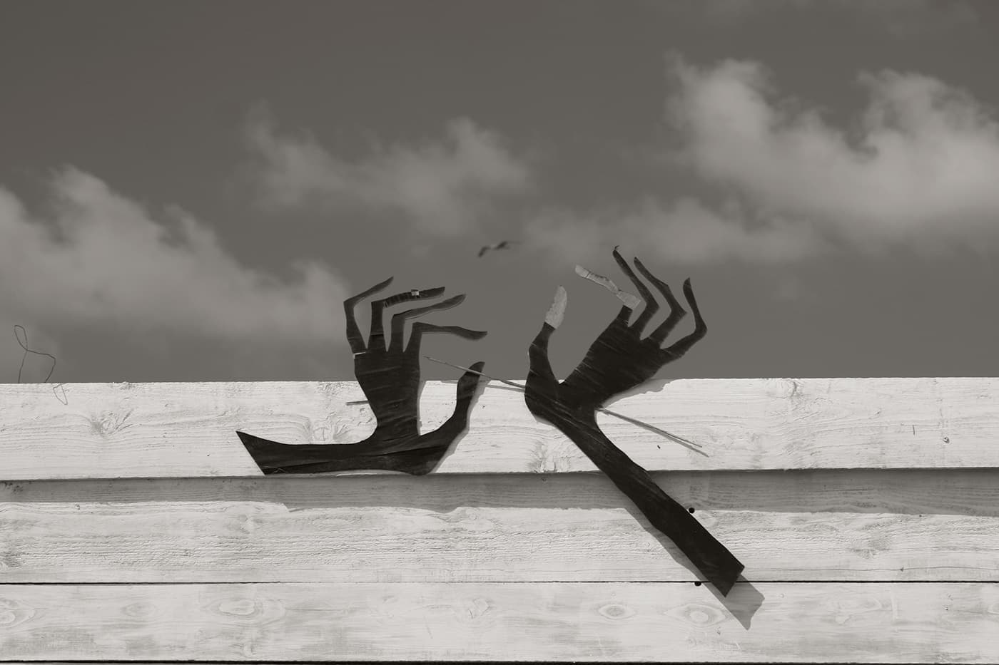 Wooden building facade with handmade cutout hands attached, reaching upward toward a bird flying in the sky above