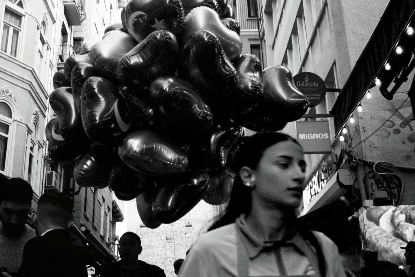 Black and white photograph of a girl walking on a street with heart-shaped balloons behind her