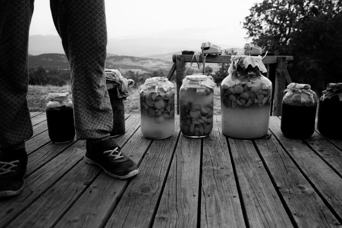 Feet of a person standing next to jars filled with pickles, fruits, and preserved food for winter
