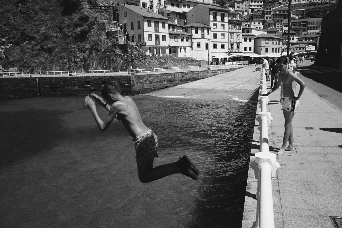 Kids near a town beach, with one child jumping into the water from a high point