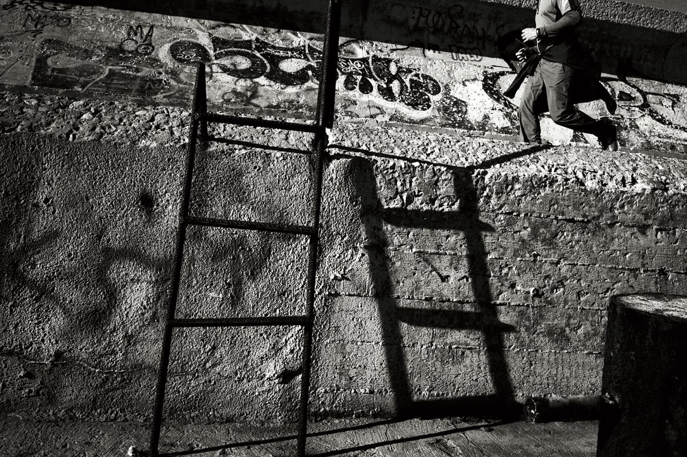 A ladder on a wall with its shadow, a man running nearby, and graffiti on the wall.