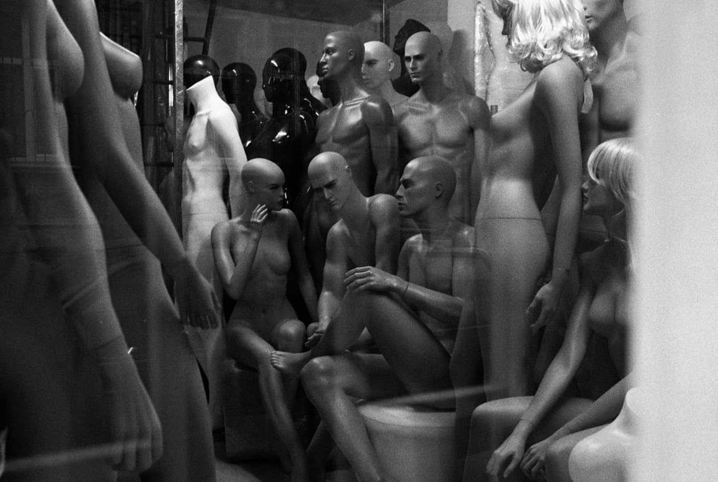 Plastic mannequins grouped together, some standing and some sitting, arranged as if they are having a discussion.