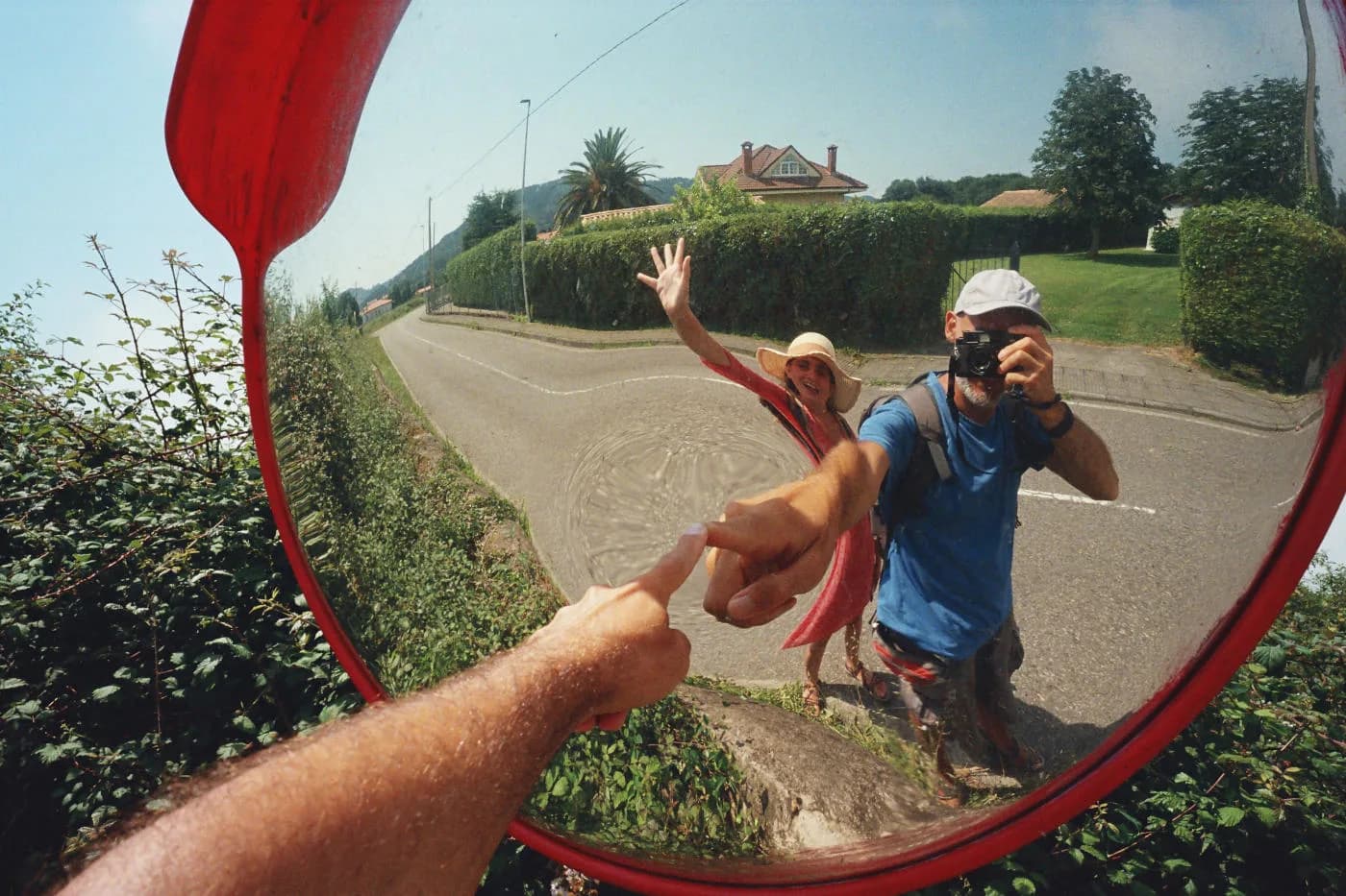 Photographer taking a photo of two people reflected in a roadside traffic mirror