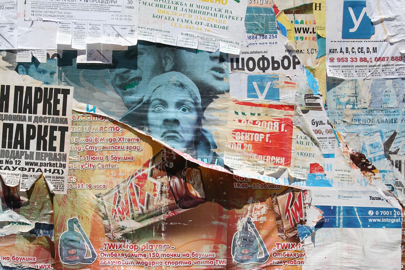 Wall covered in chaotic layered posters and advertisements, with torn sections revealing a noisia music event poster and band member faces in the center
