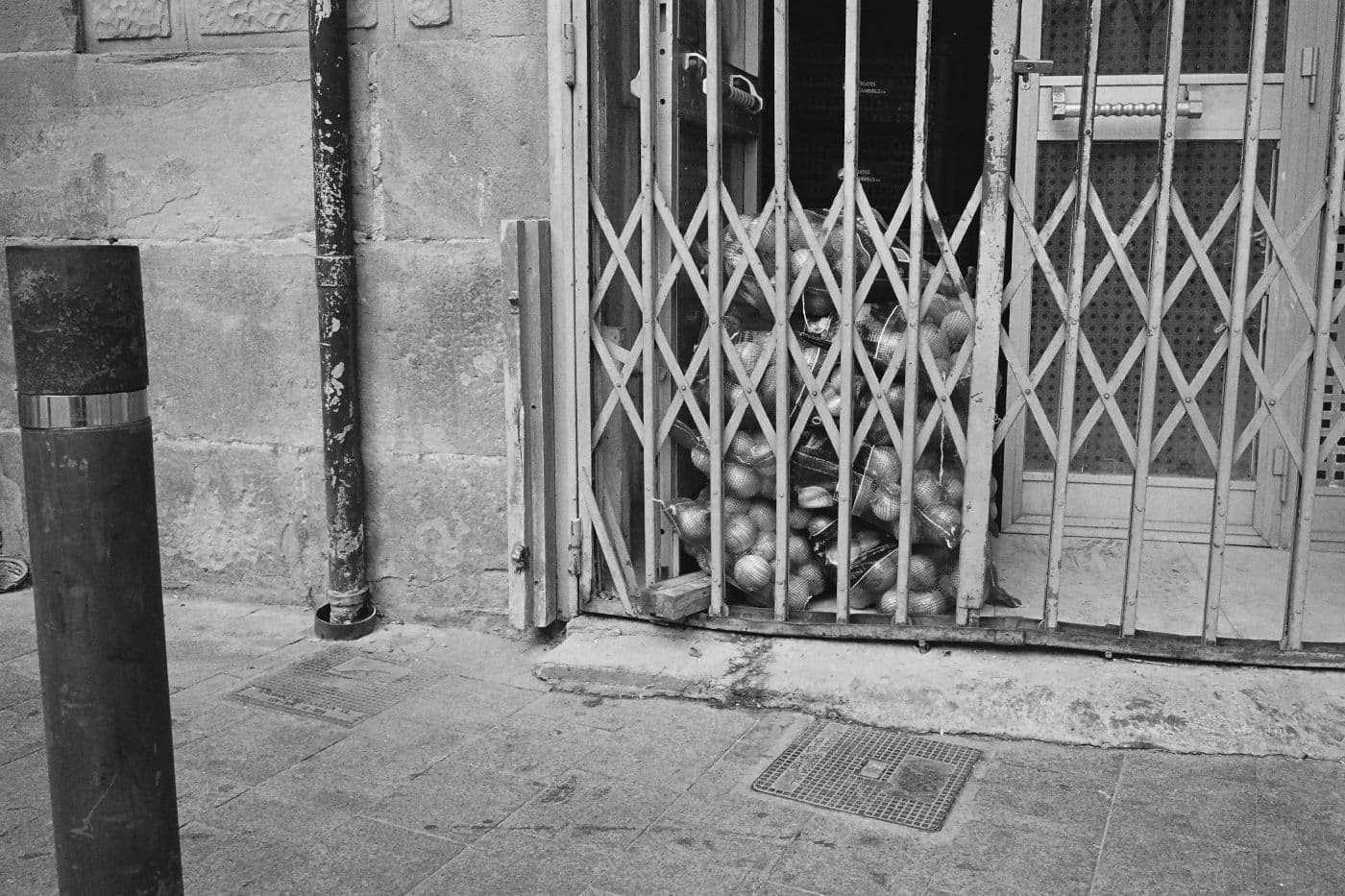 Sidewalk scene with a metal barred door embedded in the ground with large bags of onions stacked behind it
