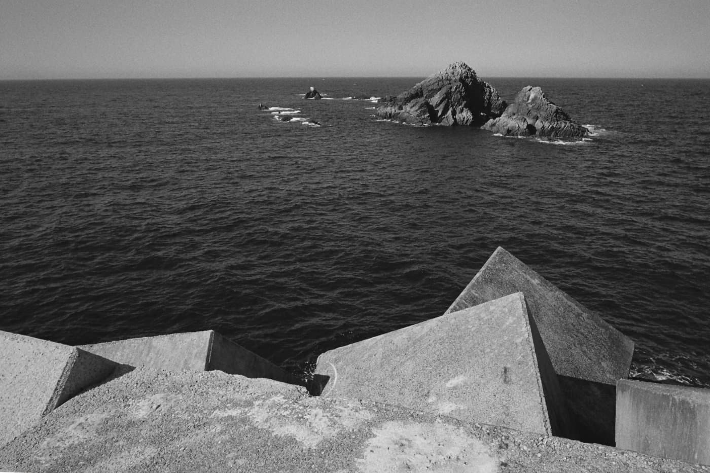 Coastline with large concrete blocks protecting the shore from waves and distant rocks rising above the ocean surface