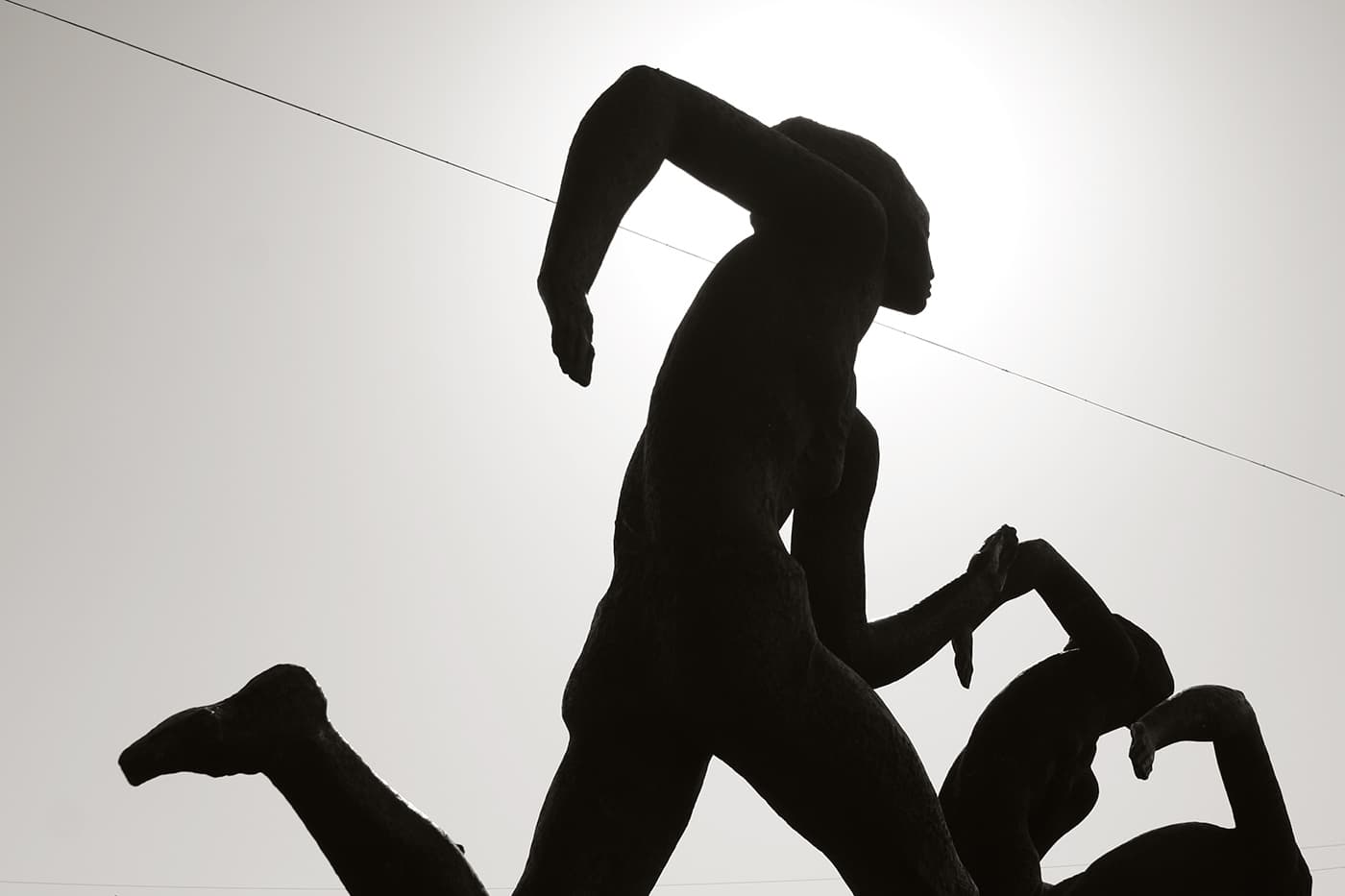 Sculptures of running men captured against the setting sun, appearing as dark silhouettes in evening light