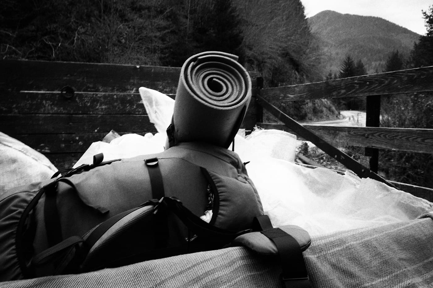 A photograph of a backpack with a sleeping pad wrapped on a truck bed with a curving road in the background.