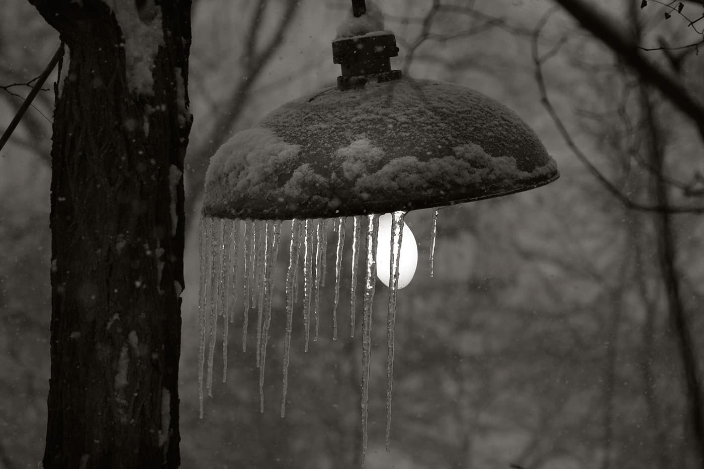 Street lamp at dusk with the light on and icicles hanging around the lampshade.