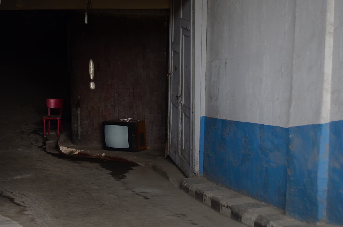 City underground parking entrance with an old television set on the sidewalk next to a chair and an exclamation mark painted on the wall above