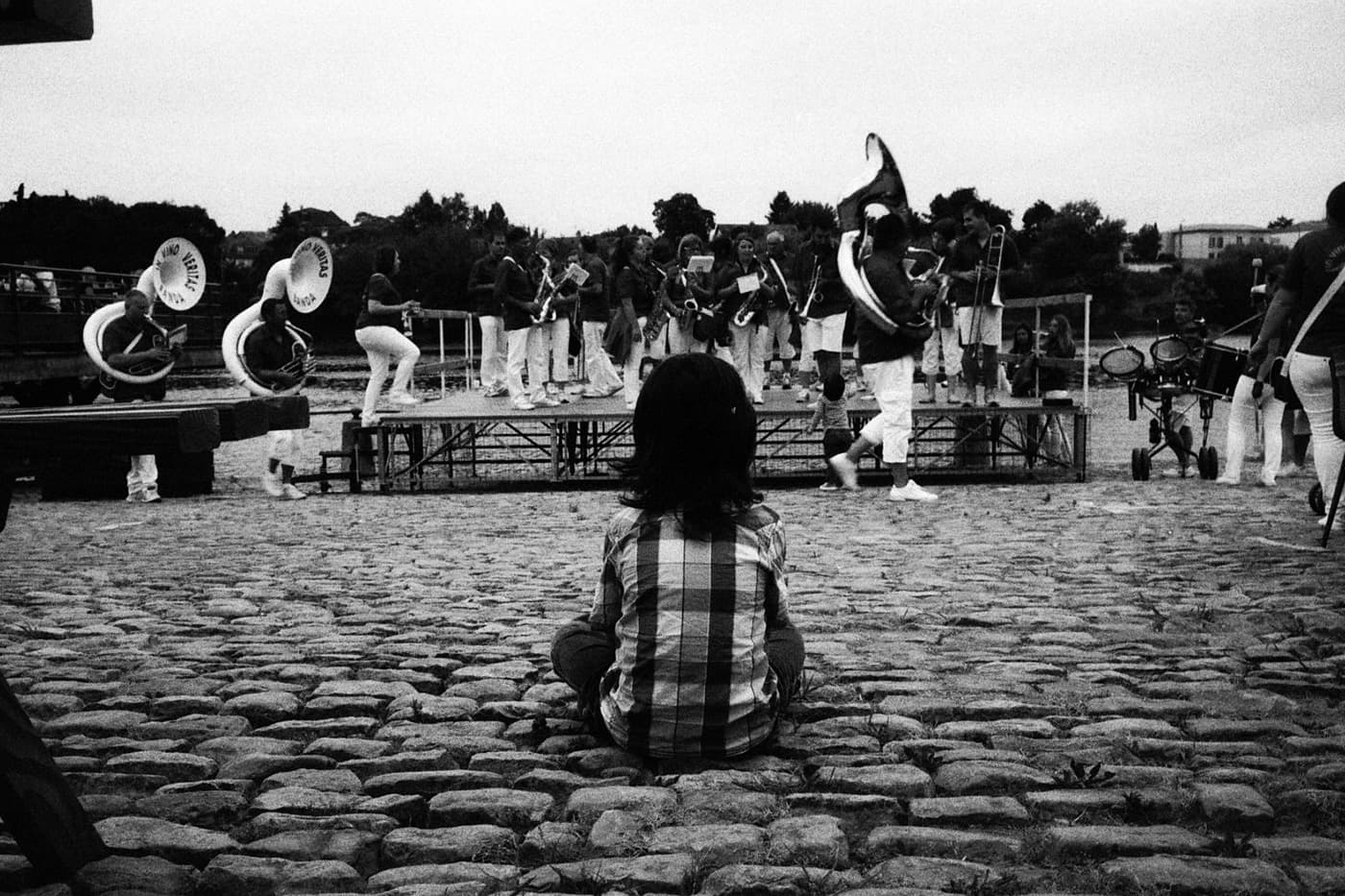 Kid seated on the ground beneath a brass band stage during an outdoor performance