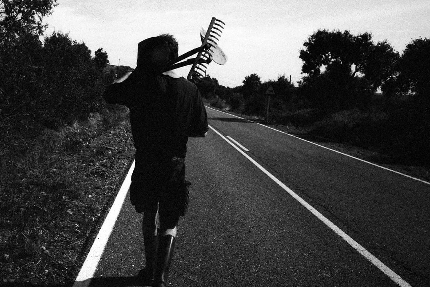 Man walking on a road carrying gardening tools on his shoulder