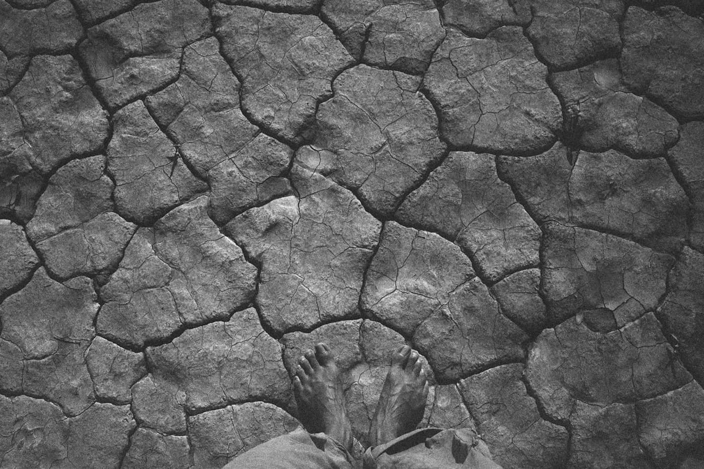 Close-up of naked feet on arid, cracked land, where the veins in the skin mirror the pattern of the dry earth beneath
