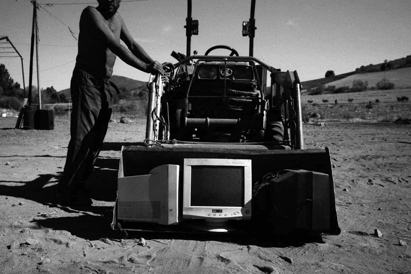Man standing next to a tractor with old computers and monitors placed in the tractor's paddle area