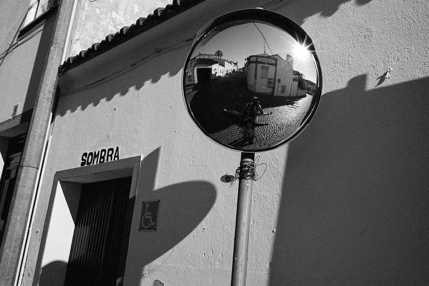 Traffic mirror at a crossroads with reflection of a street with people, buildings, and the sun low in the sky