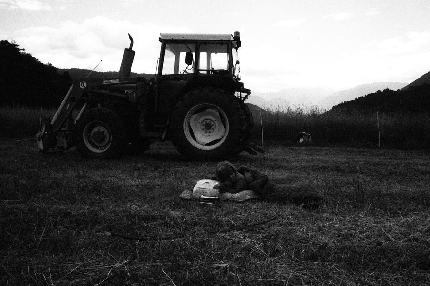 A child lying on a mattress in a grassy field next to a tractor
