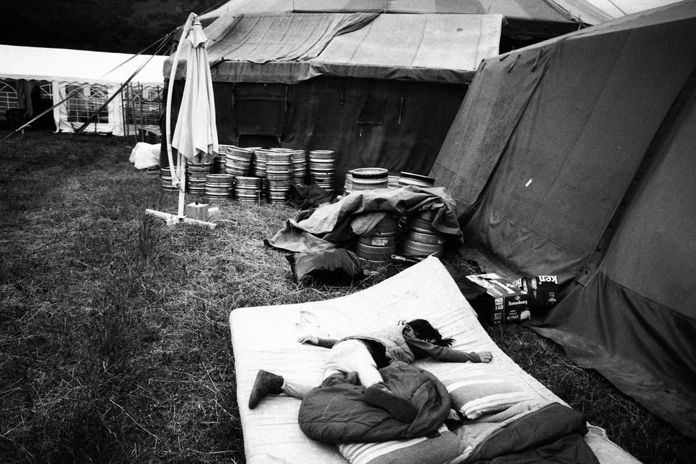 Backstage carnival area with tents, beer kegs, and a child playing on a mattress