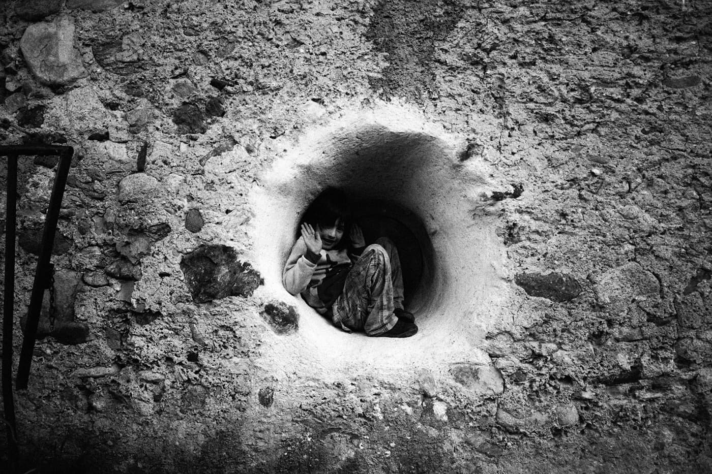 A boy curled up inside a round window opening in a stone wall
